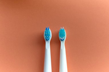 Mavi tüylü iki beyaz diş fırçasının yakın çekimi. Biri yeni diğeri ise turuncu arka planda kullanılmış..
