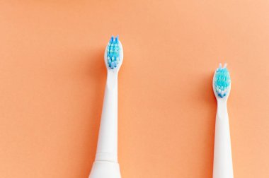 Mavi tüylü iki beyaz diş fırçasının yakın çekimi. Biri yeni diğeri ise turuncu arka planda kullanılmış..