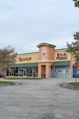 Florida, ABD - 23 Mart 2024: Deniz ürünleri restoranının yanındaki berber dükkanını gösteren renkli bir görüntü, her ikisi de canlı tabelalarla, potansiyel müşterileri çeşitli alışveriş merkezlerine davet ediyor.