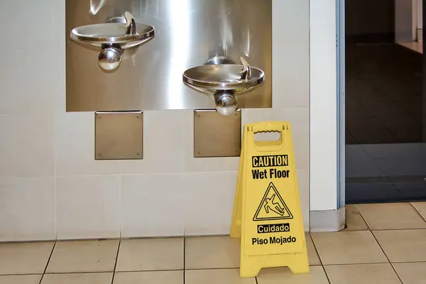 The wet floor sign in the foreground with two drinking fountains in the background captures attention to safety and accident prevention in common areas.