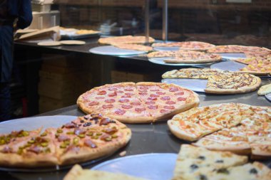Bu resim farklı malzemeli çeşitli gurme pizzaları gösteriyor, sıcak ve davetkar bir pizzacı atmosferinde servis edilmeye hazır. Pizzalar cezbedici bir şekilde düzenlenmiş, bu da kaliteli bir yemek deneyimi olduğunu gösteriyor..