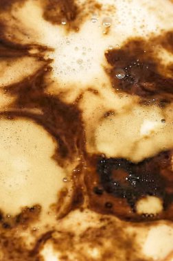 Köpüğün soyut ve sanatsal bir kalıp oluşturduğu, sıcaklık ve rahatlık hissi uyandıran bir fincan kahvenin yakın çekimi..