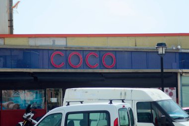 Tarragona, İspanya - 6 Nisan 2024: Tarragona şehrindeki Coco mağazasının resmi, büyük kırmızı harflerle mavi bir cepheye karşı, güneşli bir günde ön tarafa park etmiş araçlarla çekildi..