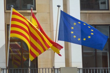A display of unity and diversity as the flags of Spain, Catalonia, and Europe wave together against the backdrop of a contemporary building. clipart