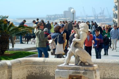 Tarragona, İspanya - 11 Nisan 2024: Bu resim, sakin okyanuslar ve arka planda hareketli kalabalıkla, hayatın karmaşasının ortasındaki birliği sembolize eden samimi bir kucaklaşmayı tasvir eden zarif bir heykeli yakalıyor..