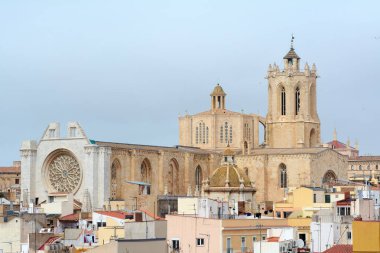 Tarragona, Spain - April 17, 2024: Featured image of the Tarragona Cathedral showcasing its historic and majestic architecture surrounded by colorful buildings under a cloudy sky. clipart