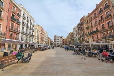Tarragona, İspanya - 22 Nisan 2024: Tarragona belediye binasına giden hareketli gezinti alanının renkli binalar ve açık hava kafeleri insanların şehir ortamının keyfini çıkardığı manzarası.