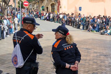 Tarragona, İspanya - 23 Nisan 2024: Arkası dönük iki sivil koruma görevlisi, kalabalık bir caddede güvenlik ve düzeni sağlayan bir etkinlik sırasında kalabalığı izliyor.