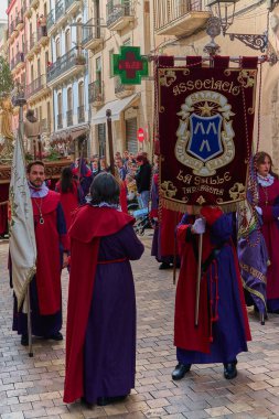 Tarragona, Spain - April 26, 2024: Authentic capture of an Easter procession on a historic street in Tarragona, showcasing participants in traditional attire and religious banners clipart