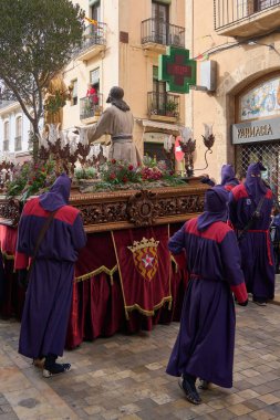 Tarragona, İspanya - 26 Nisan 2024: Tarragona 'nın tarihi bir caddesinde bir Paskalya alayının otantik bir şekilde ele geçirilmesi, geleneksel bornoz giymiş katılımcıların şamandıra taşıması.