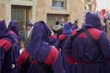 Tarragona, İspanya - 27 Nisan 2024: Tarragona, Katalonya 'nın tarihi caddelerinde düzenlenen Kutsal Hafta töreninde kırmızı cüppeli ve mor başlıklı sadık katılımcılar