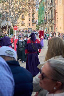 Tarragona, İspanya - 27 Nisan 2024: Tarragona, Katalonya sokaklarında canlı kutsal hafta geçidi. Tövbe edenler ve dini simgeler ciddi ve hareketli bir atmosfer yaratırlar..