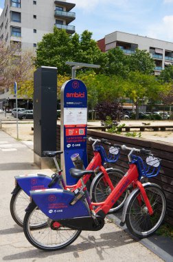 Viladecans, Barcelona, Spain-May 25, 2024: A city bike sharing station featuring blue and red bicycles ready for use. The backdrop of apartment buildings and a pedestrian. clipart