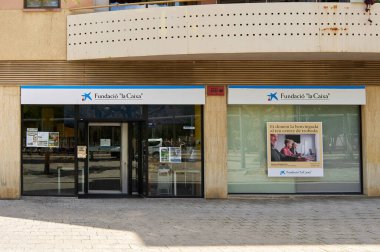 Viladecanlar, Barselona, İspanya-26 Mayıs 2024: Bir şehirdeki La Caixa Vakfı ofisinin dış görünüşü, ana girişi ve bir reklam afişi.
