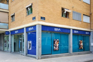 Viladecanlar, Barselona, İspanya-26 Mayıs 2024: BBVA 'nın cam girişli ve ATM' li bir banka şubesinin cephesi. Banka, yaya kaldırımı ve ön planda ahşap bir bank bulunan bir kentsel alanda yer almaktadır..