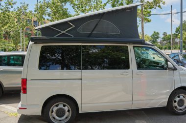Genişletilebilir çatısı olan beyaz seyahat minibüsü şehir ortamında park edilmiş, açık hava maceraları ve şehir kampı için mükemmel..