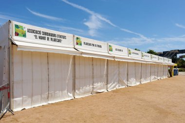 Viladecasn, İspanya - 12 Ağustos 2024: Sant Isidro Panayırı, arka planda beyaz kabinleri, ağaçları ve binaları olan, parçalı bulutlu gökyüzünün altında.