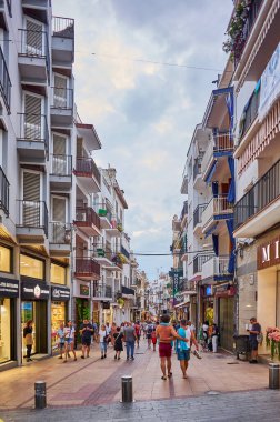 Sitges, Barcelona-Eylül 01.2024: Ziyaretçiler mağazaları ve mavi gökyüzü altındaki tipik Katalan mimarisini keşfederken rahat atmosferin keyfini çıkarıyorlar.