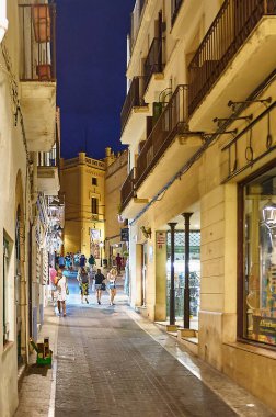 Sitges, Barcelona-Eylül 03.2024: Sitges 'de bir sokak gece görüntüsü, sokak lambalarıyla aydınlatılmış ve Akdeniz mimarisi tarafından çevrelenmiş. İspanya 'daki gecelerin güzelliğini ve sükunetini vurgulamak için mükemmel..