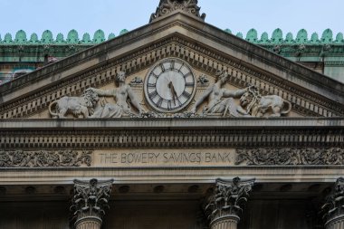 New York, United States -September 16,2024: Detailed view of the classic facade of The Bowery Savings Bank in New York, highlighting its central clock and ornamental sculptures adorning the building. Ideal for historical architecture and urban herita clipart