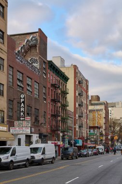 New York, ABD - 19 Eylül 2024: Tarihi binalar, park edilmiş araçlar ve şehir tabelasıyla New York caddesinin manzarası. Görüntü, parçalı bulutlu bir gökyüzü altında kentsel yaşamın özünü yakalıyor..