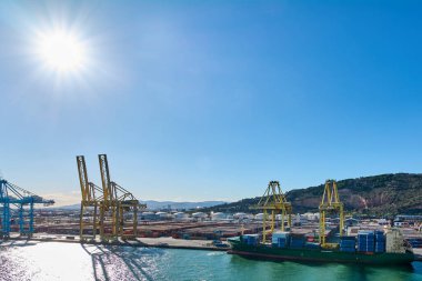 Barselona 'da. Espain - 28 Eylül 2024: Endüstriyel vinçler çalışırken Barselona Limanı 'nda büyük bir gemi boşaltılıyor. Parlak güneş ışığı sudan yansıyarak yoğun bir günü yakalar.