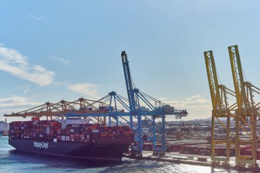 Barselona 'da. Espain - 20 Ekim 2024: Barcelona limanında vinçleri ve açık mavi gökyüzü olan konteynırlarla dolu bir kargo gemisinin görüntüsü. Lojistik ve denizcilik konuları için mükemmel.