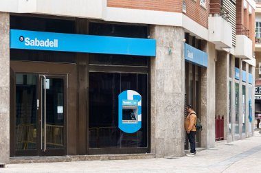 Viladecanlar. İspanya - 7 Kasım 2024: Banco Sabadell mavi işareti ve ATM ile. Bir müşteri banka şubesinin dışındaki ATM 'yi kullanıyor. Kentsel bankacılık kolaylığı kavramı..