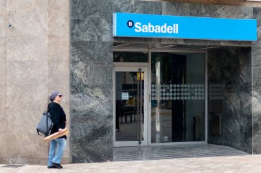 Viladecanlar. İspanya - 7 Kasım 2024: Bir Sabadell banka şubesinin önünden geçen bir yaya ile girişi, bankaların markalaşmasını ve kentleşmesini vurguluyor.