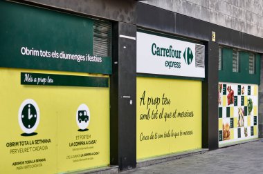Viladecanlar. İspanya - 7 Kasım 2024: Pazar ve tatiller de dahil olmak üzere her gün açık olduğunu belirten işaretli Carrefour Express mağazası. Görüntü Katalanca promosyon mesajlarını gösteriyor ve