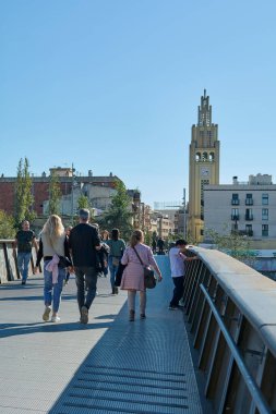 Montcada i Reixac. Spain - November 12,2024: The pedestrian bridge over the Ripoll river in Moncada and Reixac is a hub of activity, with people walking and the scenic urban and river views. clipart