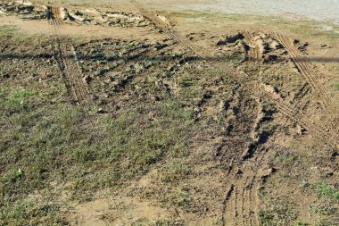 Görüntü derin araç lastik izleriyle çamurlu bir alanı gösteriyor, taşıt trafiğinin kırsal bölgeler üzerindeki etkisini ve ıslak, çamurlu zeminin dokusunu vurguluyor..