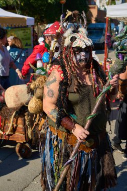 Montcada i Reixac. İspanya - 13 Kasım 2024: Bir personel ve çeşitli dekorasyonların yer aldığı karmaşık bir kostüm giysisi içindeki bir birey açık hava etkinliğinde duruyor. Kostümde renkli mantarlar ve kafatası başlığı var..