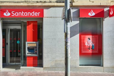 Montcada i Reixac. İspanya - 13 Kasım 2024: Santander banka şubesi belirgin modern tasarımı ve belirgin kırmızı logosuyla. Banka, bankanın varlığını ve erişilebilirliğini vurgulayarak, şubenin kalabalık bir kentsel alandaki konumunu vurguluyor.