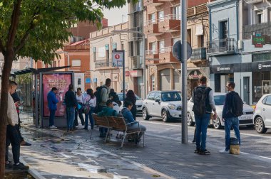 Viladecanlar. İspanya - 14 Kasım 2024: Viladecan 'da yoğun otobüs durağı, otobüsü bekleyen birden fazla kişi var. Sahne, günlük şehir yaşamını ve şehir dinamiklerinde toplu taşımanın önemini yansıtıyor..