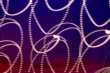 This image features intricate light trails with a beaded effect, forming looping patterns against a gradient background that transitions from deep blue to reddish hues clipart