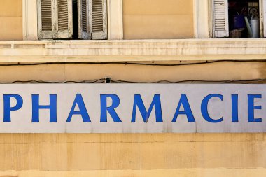 Marsilya, Fransa 'da bir eczanenin ön cephesinde, reklamının üstünde mavi bir tabela ve açık komşu pencereler var..