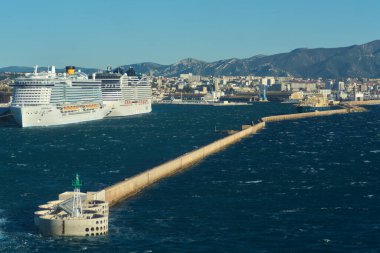 Marseille, France - December 03, 2024: Industrial wave energy converter with circular holes, protecting the Marseille coast. A green lighthouse sits at the end, with ocean waves breaking against it. clipart