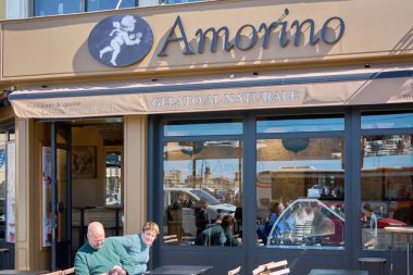 Marsilya, Fransa, 4 Aralık 2024 Amorino gelato dükkanında güneşli bir gün. Müşteriler dışarıda yemek yemeyi severler. Mağaza vitrininde Amorino logosu ve Gelato al Naturale görünüyor, rahat bir atmosfer yaratıyor..