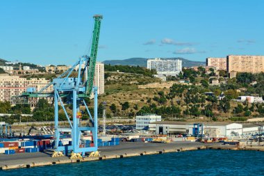Marsilya, Fransa, 4 Aralık 2024: Marsilya liman kulelerinde nakliye konteynerlerinin üzerinde büyük bir endüstriyel vinç, arka planda hareketli deniz faaliyetleri ve şehir yaşamını ön plana çıkaran kentsel binalar