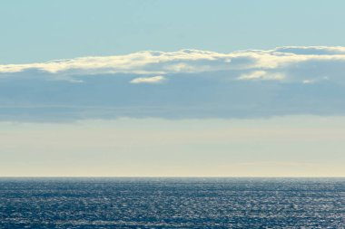 Güneş ışığının suya yansıdığı geniş bir deniz manzarası. Gökyüzü boyunca uzanan büyük, aydınlık bir bulut dinamik ve dinamik manzarayı güçlendirir..