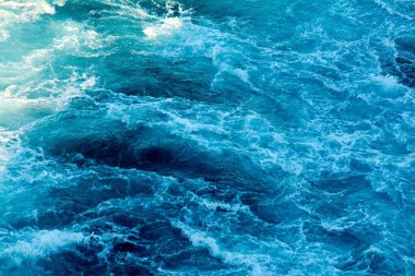 Okyanusun ham enerjisinin büyüleyici görüntüsü, derin mavi su ve köpüklü beyaz dalgalar gösteriyor, denizin dinamik ve büyüleyici güzelliğini vurguluyor.