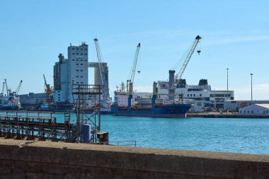 Savona. İtalya - 07 Aralık 2024: Birden fazla kargo gemisinin limana yanaştığı, vinçlerin çalıştığı ve arka planda çeşitli binaların bulunduğu hareketli bir sanayi limanı, yoğun deniz faaliyetlerini gösteriyor