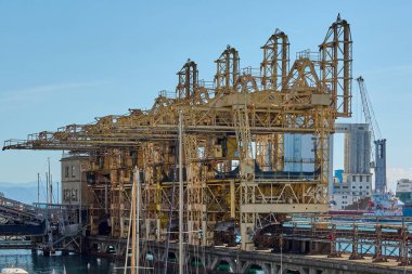 Savona, İtalya - 07 Aralık 2024: Savona limanındaki eski bir endüstriyel vinç modern yapılara karşı tarihi makineleri ön plana çıkarıyor. Endüstriyel miras ve deniz tarihi konuları için mükemmel..
