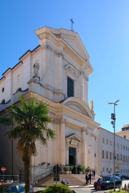 Civitavecchia. İtalya - 19 Aralık 2024: Civitavecchia, İtalya şehir sokak manzarası, açık mavi gökyüzü altında tarihi bir kilise ve modern binalar sergileniyor: Şehir hayatı, mimari karşıtlık