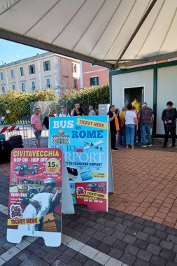 Civitavecchia, Italy - December 19, 2024: People stand in line at a ticket booth under a canopy, buying tickets for bus services to Rome, Fiumicino Airport, and hop-on hop-off tours. clipart