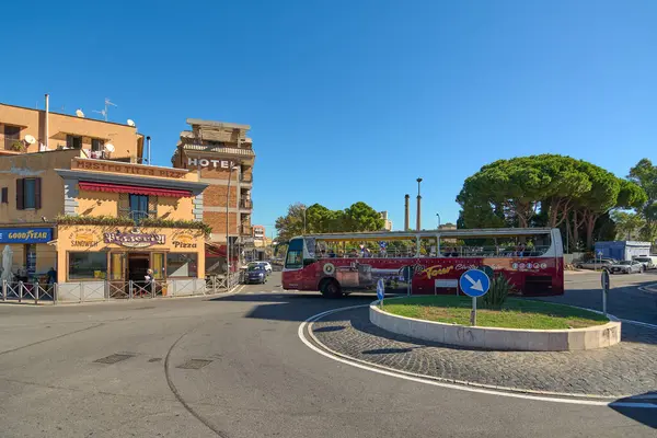 Civitavecchia, İtalya - 19 Aralık 2024: Civitavecchia 'da bir döner kavşakta üzerinde pizzacı ve otel konsepti olan binaların önünden geçen bir tur otobüsü: kentsel turizm ve ulaşım