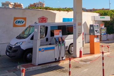 Civitavecchia. Italia - 27 Aralık 2024: Benzin istasyonunda beyaz bir minibüs. Güneşli bir günde birden fazla pompa ve yangın söndürücü görünür. Kavram: Kentsel yakıt istasyonu.