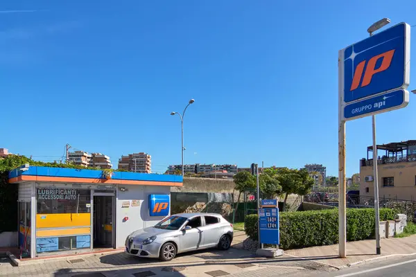 Civitavecchia, Italia - 27 Aralık 2024: Parlak mavi bir gökyüzü altında kentsel bir ufuk çizgisi tarafından çerçevelenmiş modern bir arabası ve açık tabelalı bir benzin istasyonu. Konsept: Şehir yaşamı ve ulaşım temel gereksinimleri.