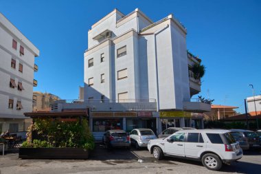 Civitavecchia. İtalya - 27 Aralık 2024: Gri cepheli, pencereli ve zemin kattaki mağazaları olan çok katlı bir bina. Arabaları önlerine ve mavi gökyüzüne park etmiş. Kavram: Kentsel mimari ve ticaret.